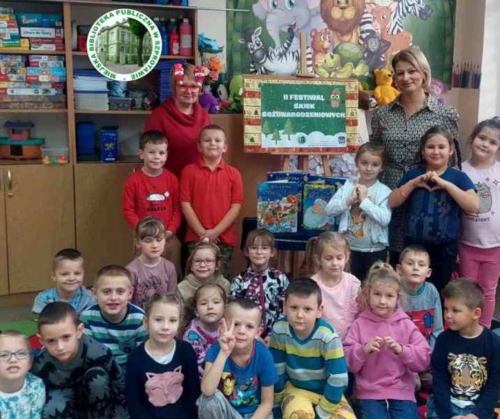 zdjęcie grupy przedszkolaków z wychowawczynią i bibliotekarką oraz plakatem 2 edyci festiwalu bajek bożonarodzeniowych