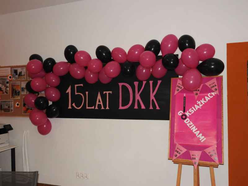 zdjęcie tablicy magnetycznej z napisem 15 lat DKK otoczonej balonami oraz plakatem projektu na stelażu