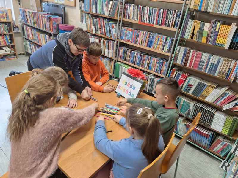 zdjęcie bibliotekarki i dzieci sięgających po kredki na stoliku