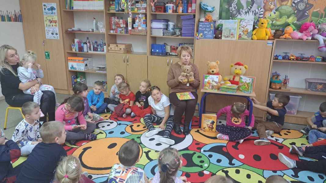 zdjęcie bibliotekarki pokazującej dzieciom na dywanie pluszowe misie i książeczki o niedźwiadkach
