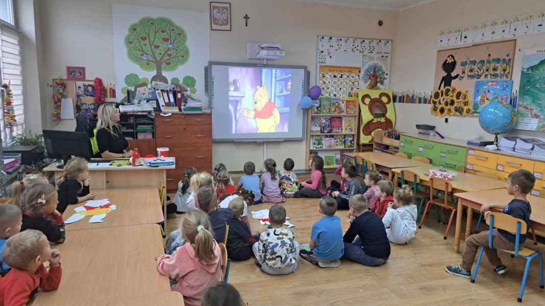 zdjęcie dzieci siedzących na podłodze w sali podczas oglądania na ekranie obrazka misia Kubusia Puchatka