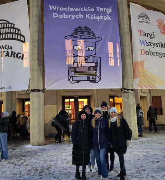 zdjęcie grupowe uczestniczek wydarzenia przed budynkiem, nad nimi baner z napisem wrocławskie targi dobrych książek