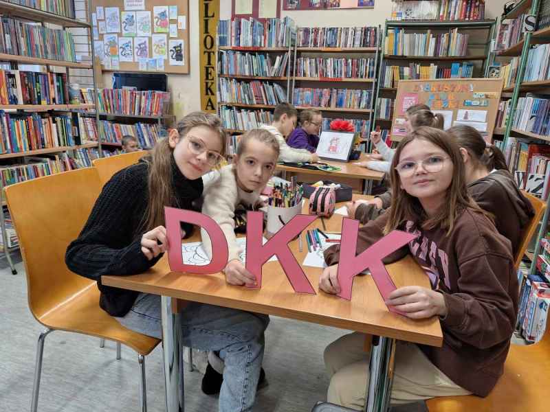 zdjęcie dziewczynek trzymających napis DKK, reszta młodzieży z tyłu przy stoliku