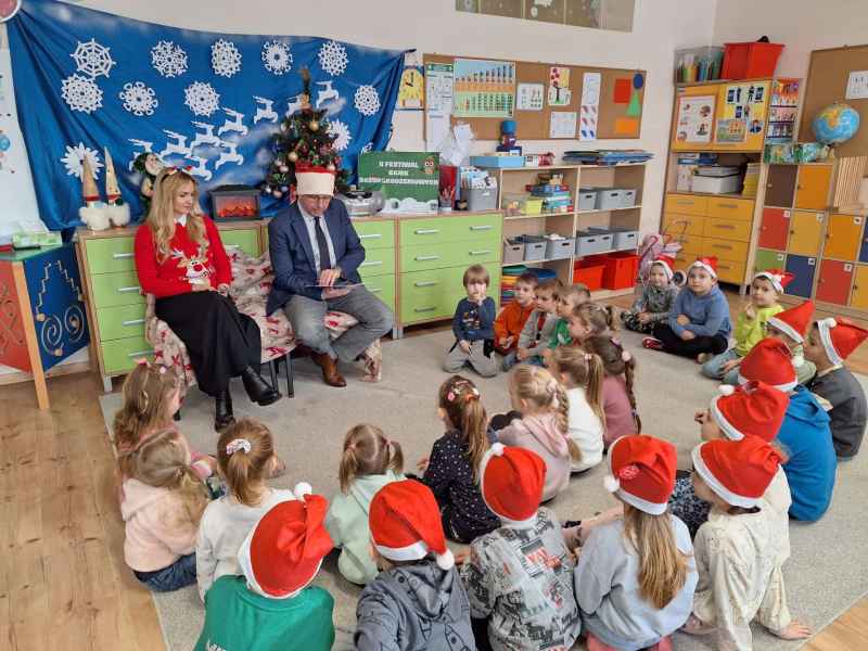 zdjęcie dyrektor biblioteki, dzieci i burmistrza czytającego dzieciom książkę