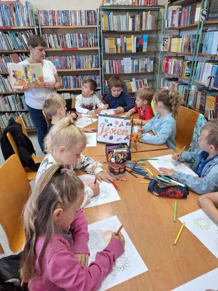 zdjęcie bibliotekarki z książką i dzieci kolorujących rysunki