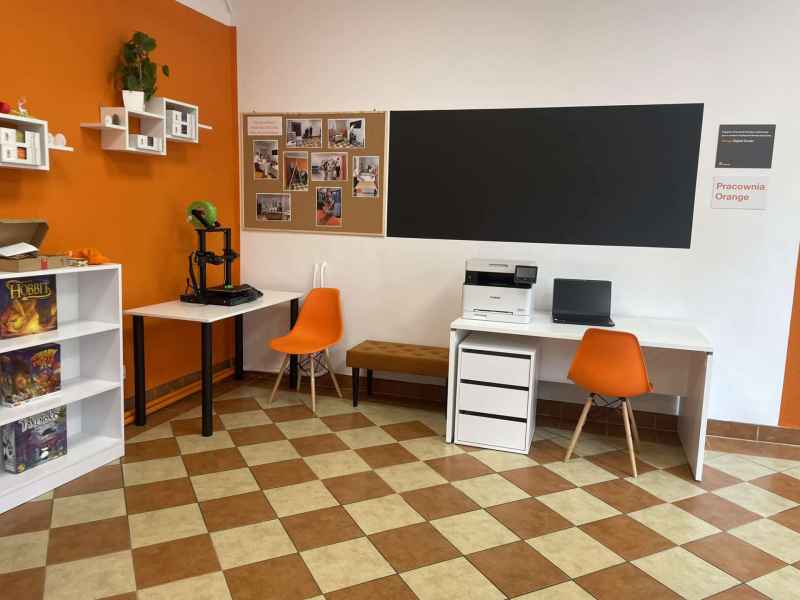 zdjęcie pomieszczenia pracowni z widocznym biurkiem, drukarką 3D, regałami z grami i tablicami