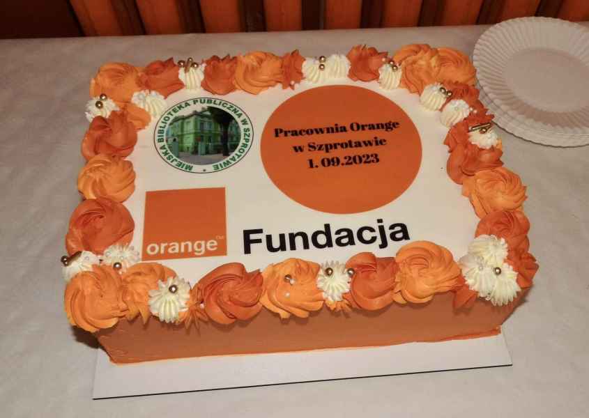 zdjęcie pomarańczowego tortu z logo biblioteki oraz fundacji Orange wrac z napisem Pracownia Orange w Szprotawie 1 września 2023