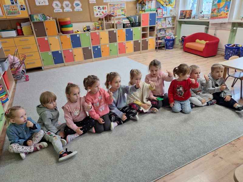 zdjęcie przedszkolaków siedzących na dywanie i pokazujących palce