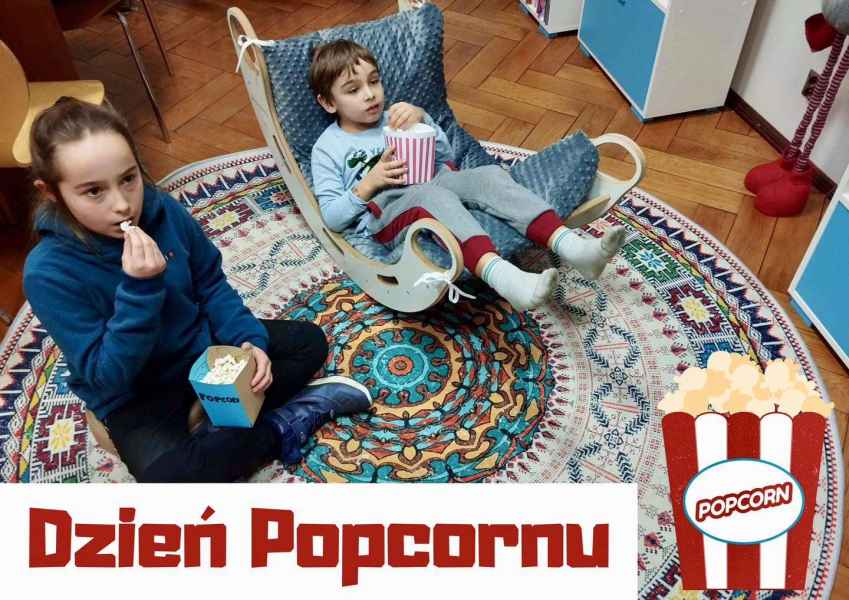 zdjęcie dwójki dzieci w trakcie jedzenia popcornu na dywanie, na dole napis dzień popcornu i obrazek kartonika z prażoną kukurydzą