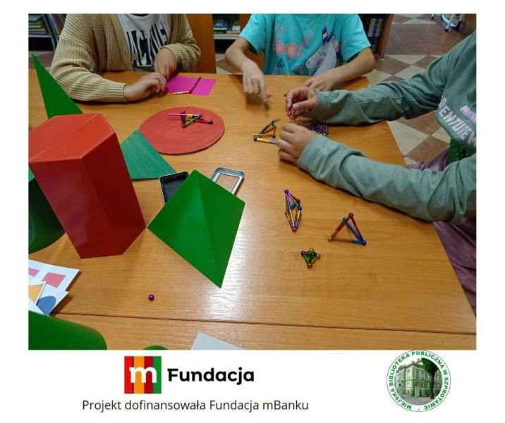 zdjęcie dzieci podczas budowania ze słomek magnetycznych, na dole logo biblioteki i mfundacji z napisem projekt dofinansowała fundacja mbanku