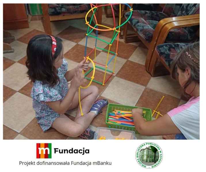 zdjęcie dziewczynek budujących ze słomek konstrukcyjnych, na dole logo biblioteki i mfundacji z napisem projekt dofinansowała fundacja mbanku