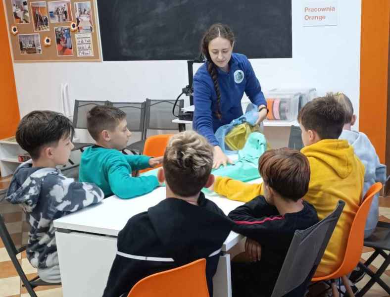 zdjęcie bibliotekarki podczas pokazywania chlopcom worków do segregacji