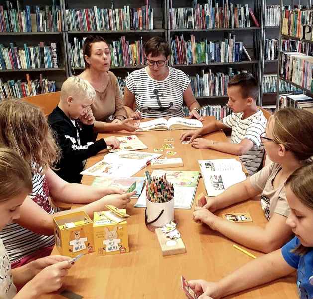 zdjęcie bibliotekarki i nauczycielki przy stoliku z dziećmi i elementarzami