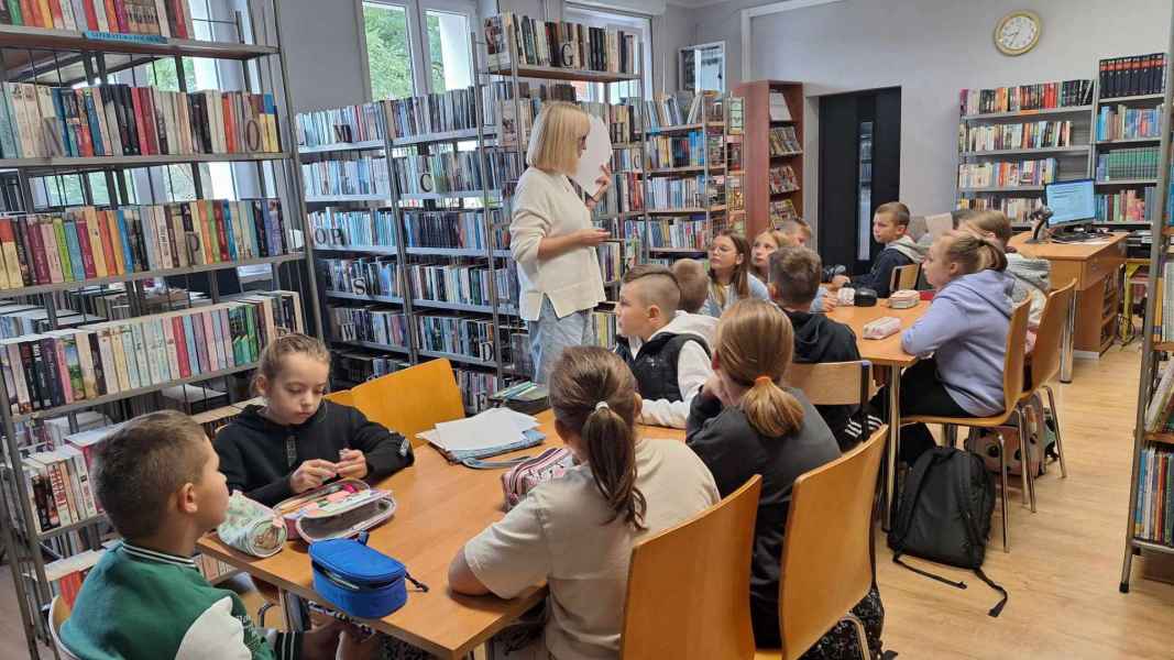 zdjęcie nauczycielki matematyki mówiącej do dzieci siedzących przy stolikach w bibliotece