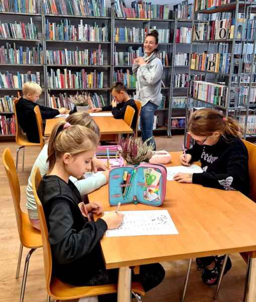 zdjęcie grupy dzieci przy dwóch stolikach podczas rozwiązywania zadań matematycznych, w tle nauczycielka