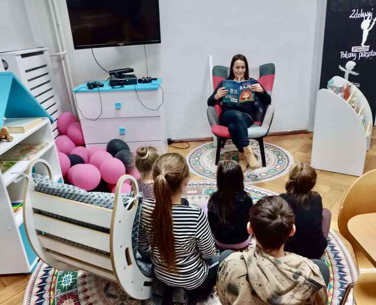 zdjęcie bibliotekarki czytającej w fotelu książkę dzieciom siedzącym na podłodze w wyremontowanej sali dla dzieci