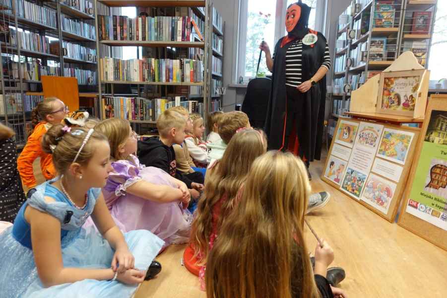 zdjęcie dzieci w bajkowych strojach siedzących na podłodze i słuchających bibliotekarki przebranej za diabła