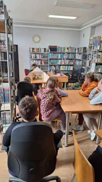 zdjęcie bibliotekarki prezentującej teatrzyk kamishibai oraz dzieci oglądających spektakl