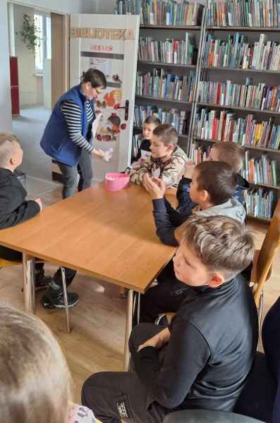 zdjęcie bibliotekarki rozdającej dzieciom zagadki na karteczkach