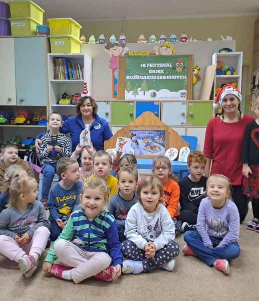 zdjęcie bibliotekarek i przedszkolaków z teatrzykiem kamishibai i plakatem 3 edycji Festiwalu Bajek Bożonarodzeniowych