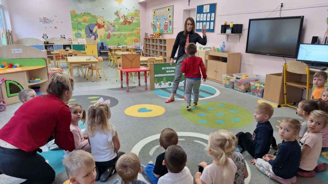 zdjęcie bibliotekarki przybijającej piątkę z chłopcem, reszta dzieci ogląda na dywanie