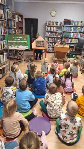 zdjęcie dzieci siedzących na podłodze i oglądających bibliotekarkę podczas prezentacji bajki z teatrzyku kamishibai