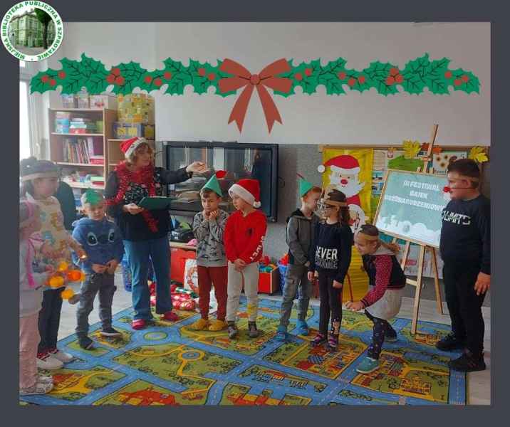 zdjęcie bibliotekarki instuującej dzieci podczas zabawy z akcesoriami świątecznymi, w tle plakat projektu, po lewej logo biblioteki, na górze grafika ostrokrzewu z kokardą