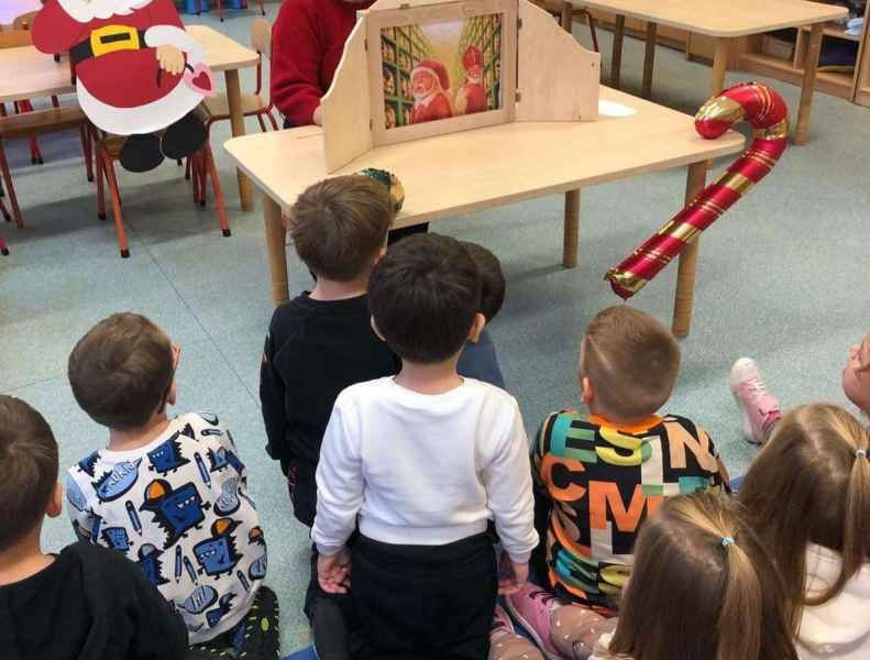 zdjęcie bibliotekarki z teatrzykiem kamishibai i dzieci oglądających spektakl