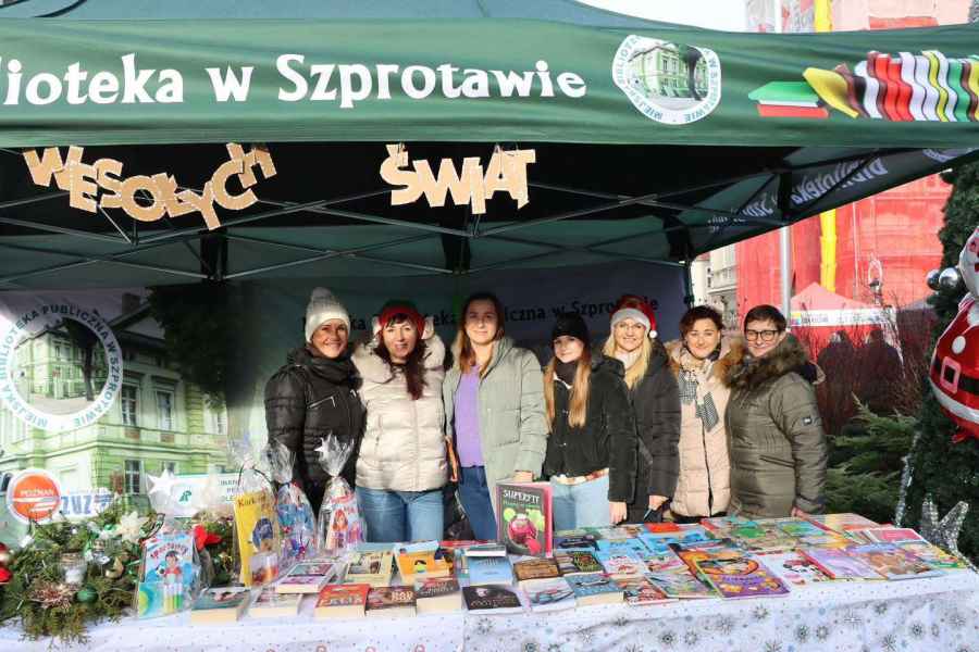 zdjęcie bibliotekarek przy stoisku biblioteki na jarmarku, na górze napis z kartonu wesołych świąt