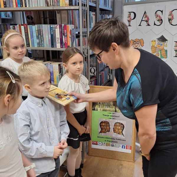 zdjęcie bibliotekarki pasującej książką chłopca na czytelnika