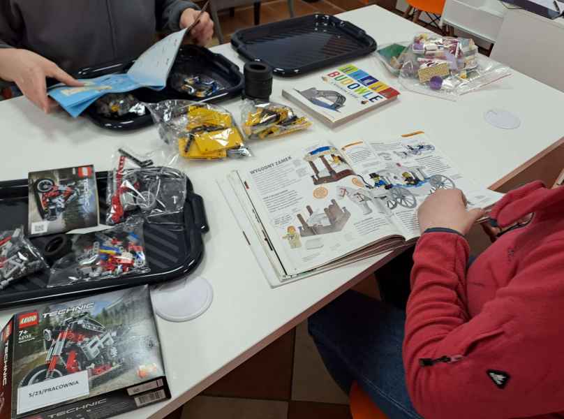 zdjęcie dzieci podczas oglądania książek i prasy przy stolikach z rozłożonymi klockami lego