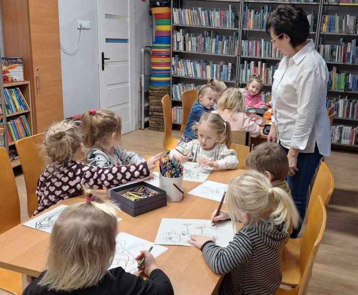 zdjęcie dzieci kolorujących obrazki przy stolikach, obok wychowawczyni 