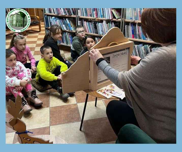 zdjęcie bibliotekarki z teatrzykiem i obserwujących dzieci, po lewej logo biblioteki