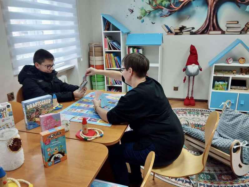 zdjęcie bibliotekarki podczas gry w grę planszową z czytelnikiem w oddziale dla dzieci