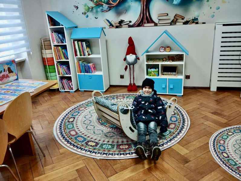 zdjęcie dziecka w bujaku na oddziale dziecięcym, w tle nowe regały i fototapeta drzewa z książkami