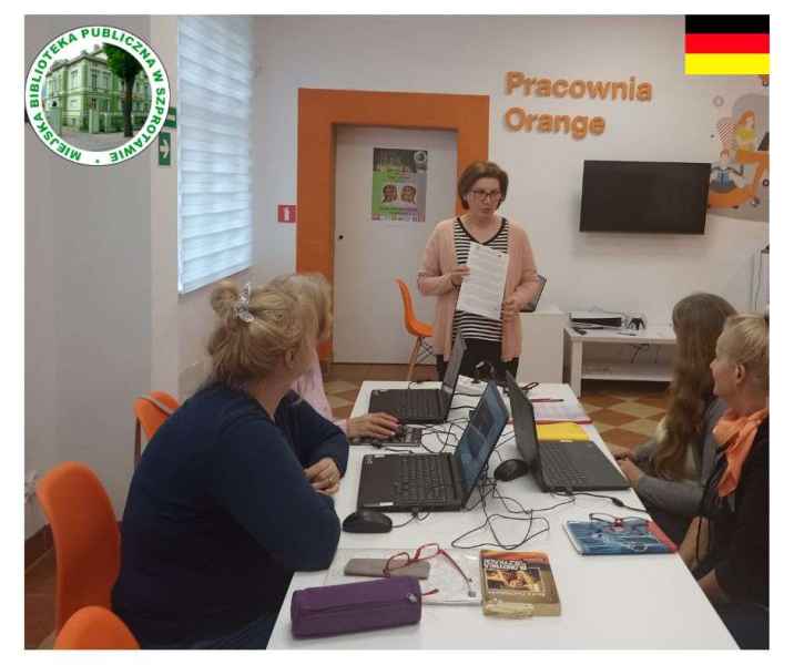 zdjęcie bibliotekarki mówiącej do czytelników przy stoliku z laptopami, po lewej stronie logo biblioteki, po prawej flaga Niemiec