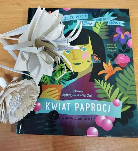 zdjęcie papierowych kwiatów na tle okładki książki "Kwiat paproci" R. Jędrzejowskiej Wróbel