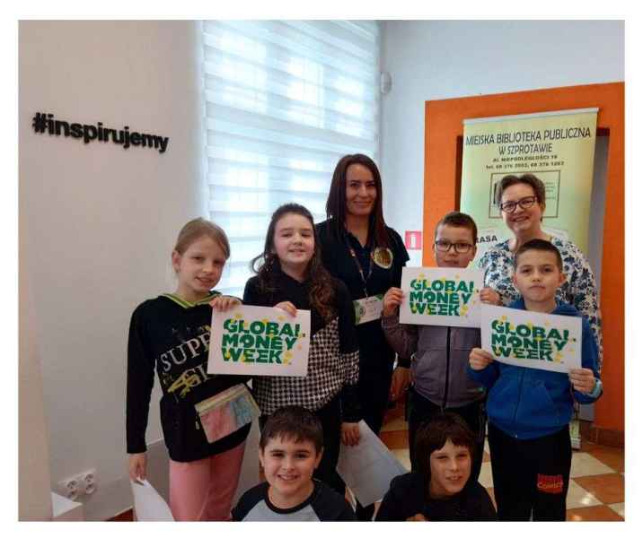 zdjęcie dzieci z bibliotekarką i wychowawczynią trzymających kartki z logo projektu global money week
