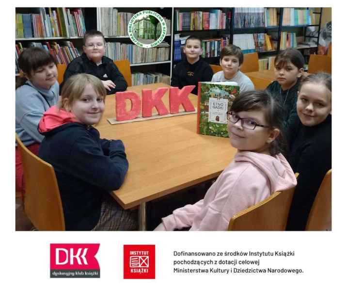 zdjęcie dzieci przy stoliku z książką i napisem DKK, na górze logo biblioteki, na dole logotypy patronów