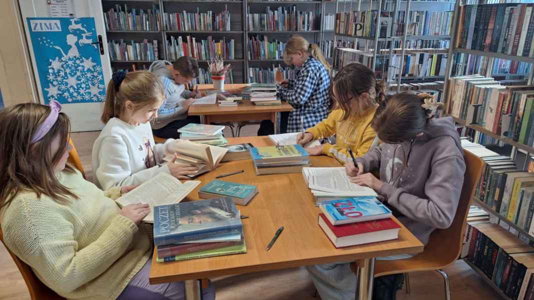 zdjęcie dzieci przy stolikach w bibliotece, przekreślają pieczątki i ubytkują część księgozbioru