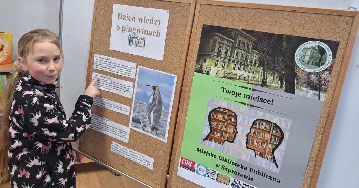 zdjęcie dziewczynki przy tablicy korkowej z informacjami na temat pingwinów, obok plakat biblioteki