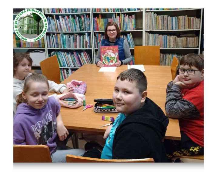 zdjęcie bibliotekarki z książką i dziećmi przy stoliku po lewej logo biblioteki