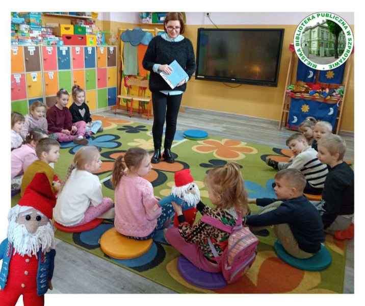 zdjęcie dzieci siedzących na dywanie z maskotką krasnala, przed nimi stoi bibliotekarka, po prawej logo biblioteki