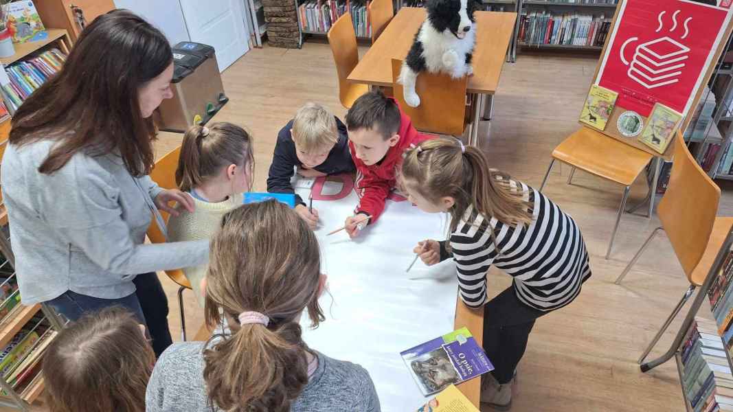 zdjęcie dzieci przy stoliku z brystolem, obok wychowawczyni i książka