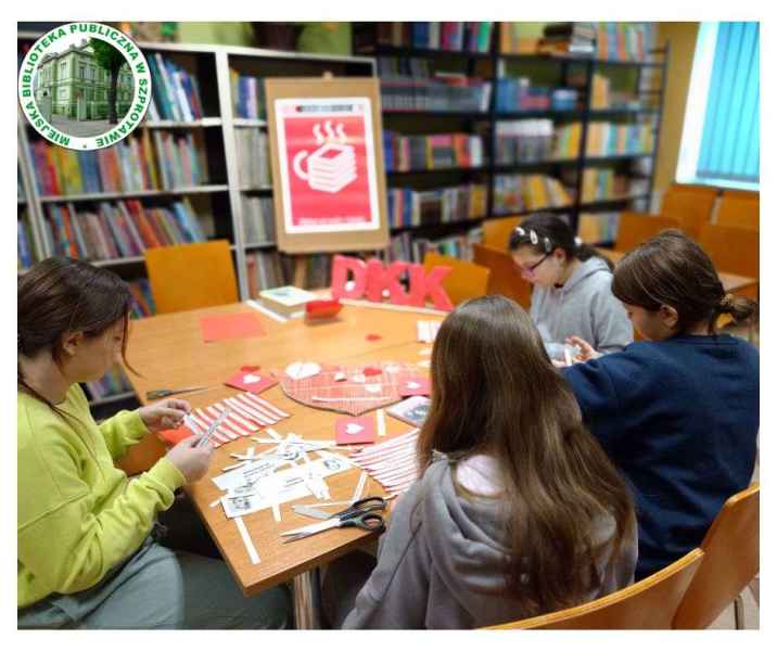 zdjęcie dzieci podczas układania i klejenia fragmentów wierszy przy stoliku, po lewej logo biblioteki