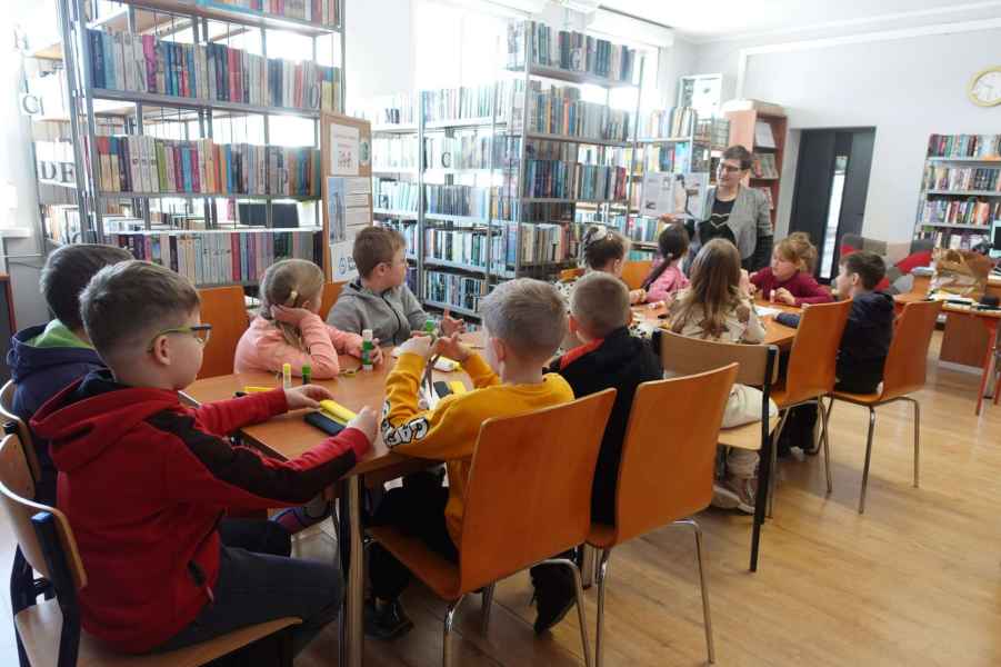 zdjęcie bibliotekarki mówiącej do dzieci siedzących przy stolikach