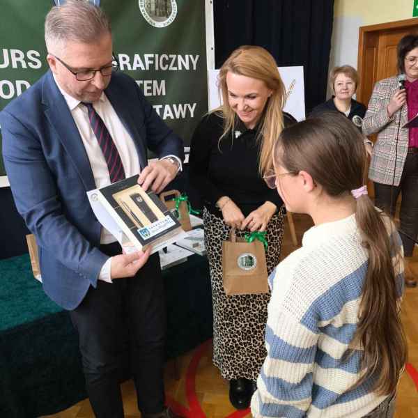 zdjęcie burmistrza i dyrektor biblioteki wręczających nagrodę zwyciężczyni konkursu 