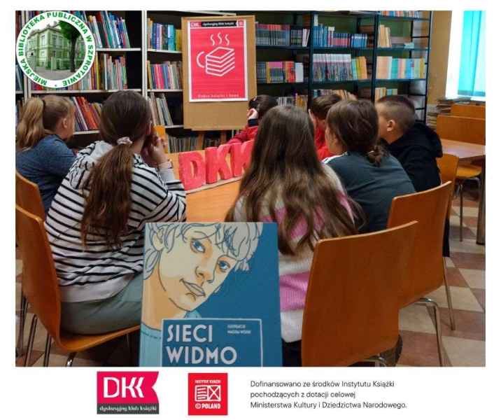 zdjęcie młodzieży patrzącej na plakat DKK, na przodzie okładka książki sieci widmo, po lewej logo biblioteki, na dole logo DKK, instytutu książki i informacja o dofinansowaniu ze środków instytutu książki