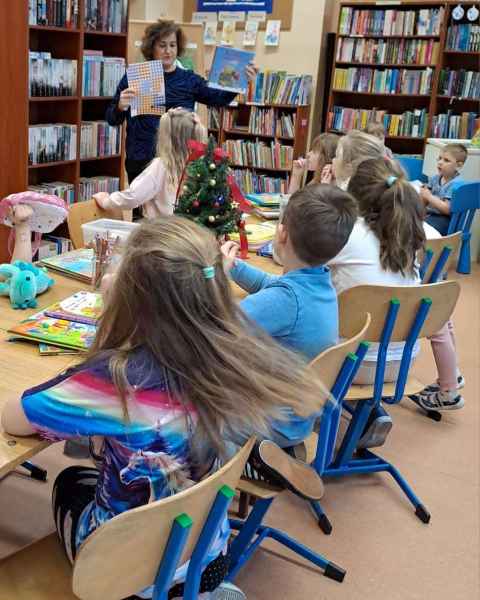 zdjęcie dzieci przy stoliku słuchających bibliotekarki