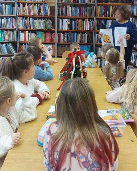 zdjęcie dzieci przy stoliku i bibliotekarki z kartkami o dniu kubusia puchatka